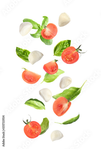 Fototapeta Naklejka Na Ścianę i Meble -  Mozzarella cheese balls, tomatoes and basil leaves falling on white background. Caprese salad