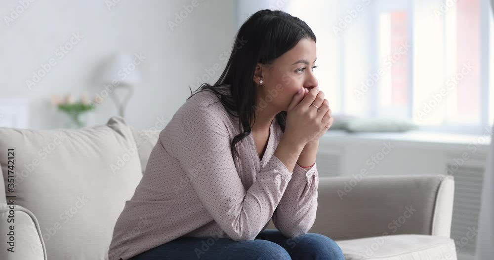 Frustrated african ethnicity young woman sitting on couch, thinking of personal problems alone at home. Depressed unhappy mixed race lady suffering from mental stress, feeling unsure of decision. Frustrated african ethnicity young woman sitting on couch, thinking of personal problems alone at home. Depressed unhappy mixed race lady suffering from mental stress, feeling unsure of decision.