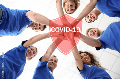 Volunteers uniting to help during COVID-19 outbreak. Group of people holding hands together on light background, shield illustration