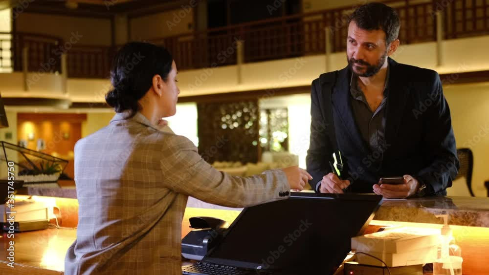 Businessman checking in at hotel. Young handsome man and receptionist at counter reception desk. Businessperson filling out information form at the front desk reception