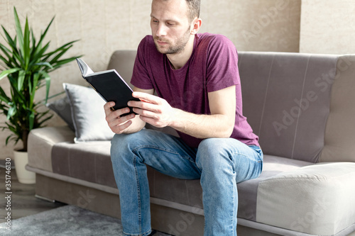 young calm man reads a book while sitting on a sofa