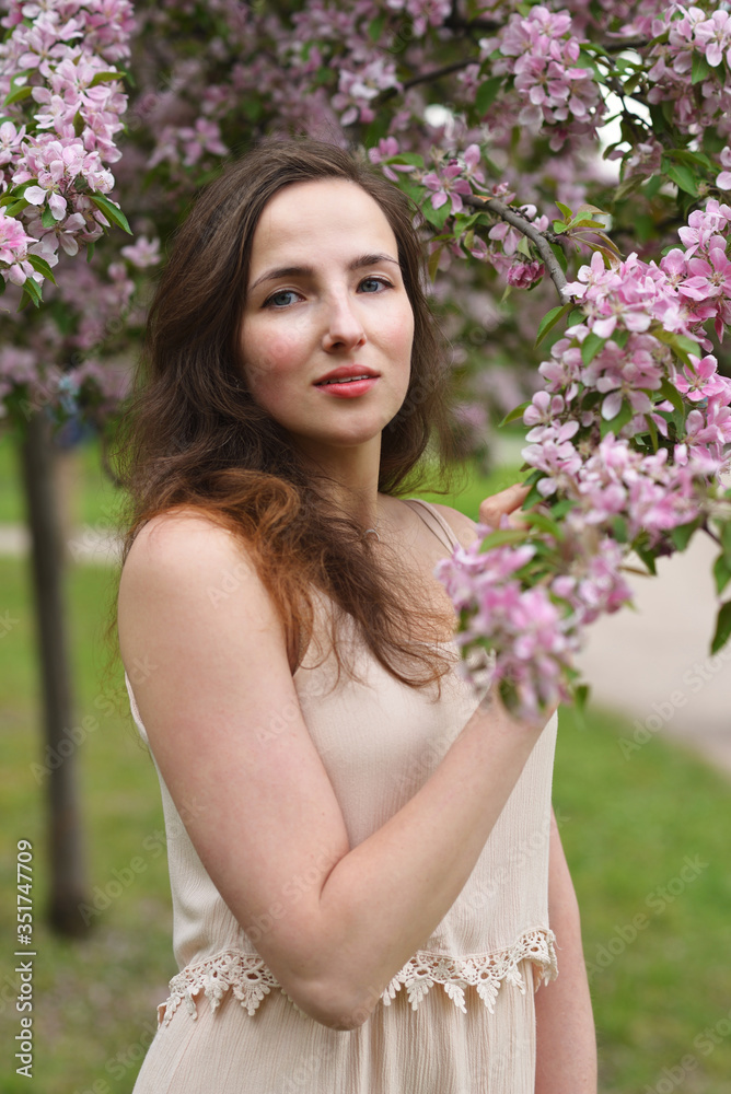 A young beautiful woman with a slight smile touches a blooming branch of an Apple tree A young beautiful woman with a slight smile touches a blooming branch of an Apple tree