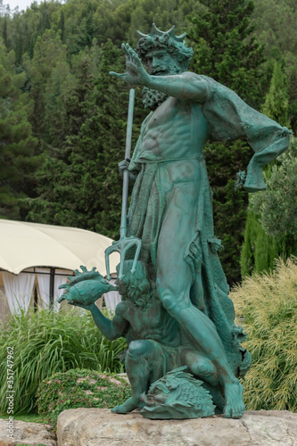 Obraz na płótnie Alushta, Russia - July 29, 2016: Statue of Neptune in the Aivazovsky landscape park in Partenit in Crimea against the backdrop of evergreen and flowering shrubs. w salonie