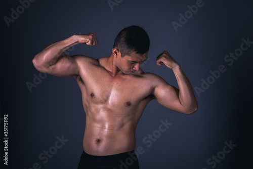 Muscular model Asian young man on Gray background. Portrait of strong brutal guy with trendy hairstyle. Sexy naked torso, six pack abs. Male flexing his muscles. Sport workout bodybuilding concept. © NITIKAN T.