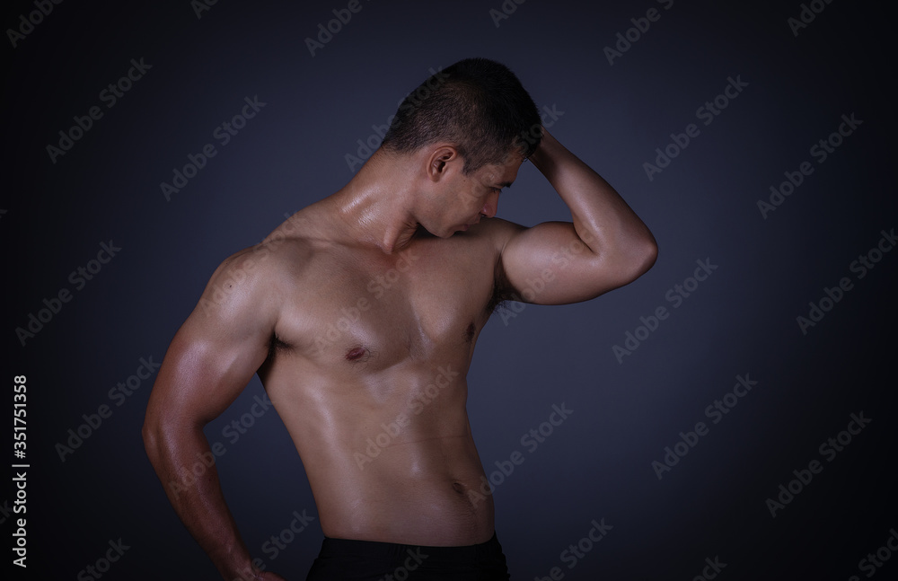 Fototapeta premium Muscular model Asian young man on Gray background. Portrait of strong brutal guy with trendy hairstyle. Sexy naked torso, six pack abs. Male flexing his muscles. Sport workout bodybuilding concept.
