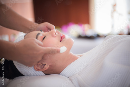 Spa and beauty room, black face mask of mud and algae, an Asian woman lying on the bed, waiting for a mask expert on a beautiful face.