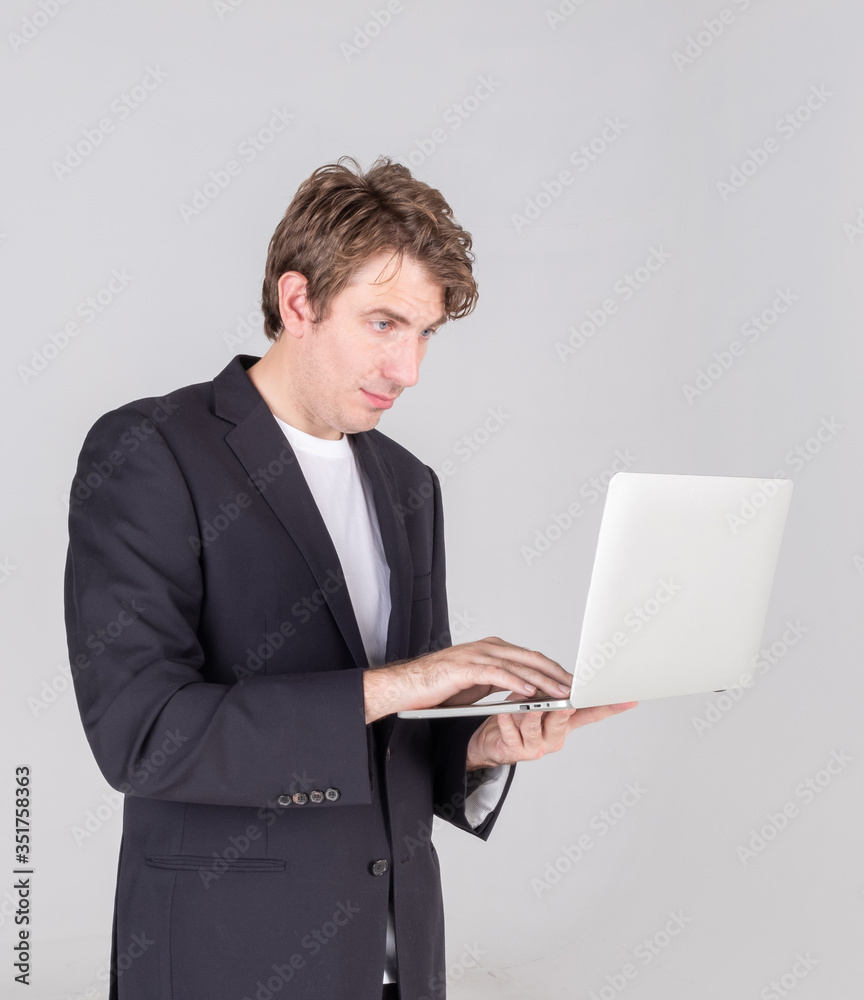 Portrait of handsome young businessman standing holding using laptop computer and checking email or confused more data, isolated on grey background. Portrait of handsome young businessman standing holding using laptop computer and checking email or confused more data, isolated on grey background.