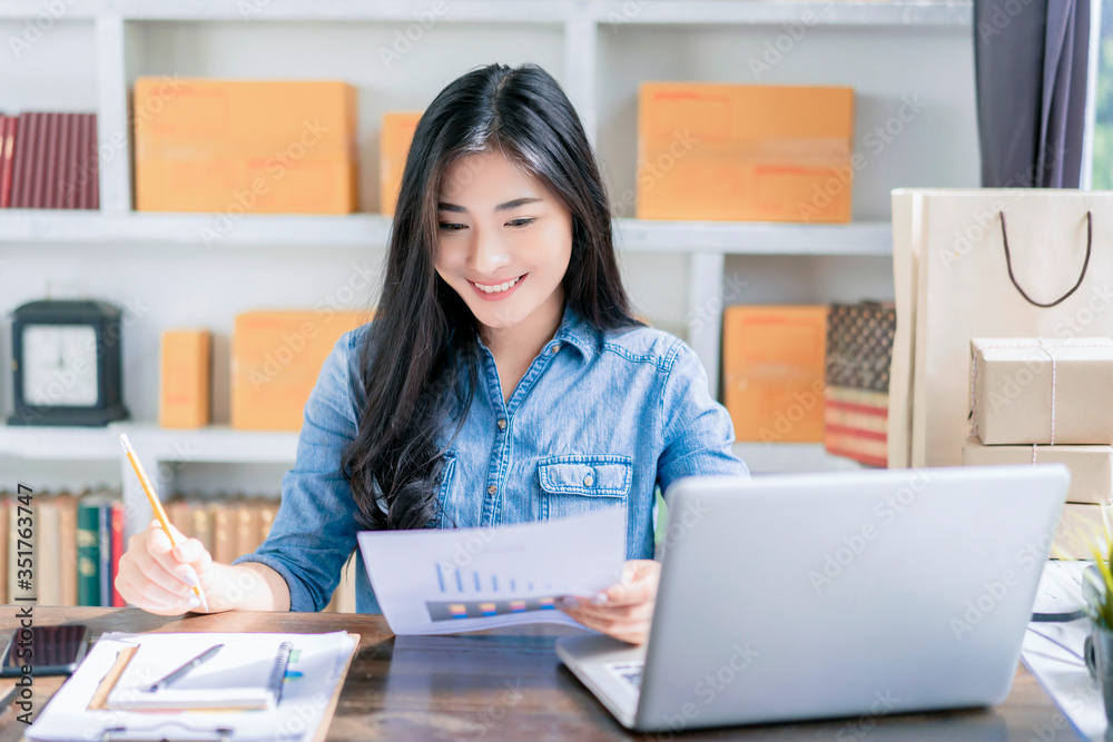 beautiful Asian businesswoman smiling writing on notebook checking statistics, using computer laptop ecommerce online store selling delivering products work at home office during quarantines isolation beautiful Asian businesswoman smiling writing on notebook checking statistics, using computer laptop ecommerce online store selling delivering products work at home office during quarantines isolation