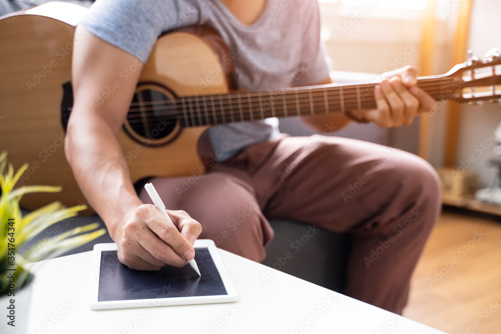 Fototapeta premium Work from home playing guitar writing composing songs free time spending activity using laptop wearing face mask self isolation quarantine lockdown staying safe in protection from coronavirus covid-19