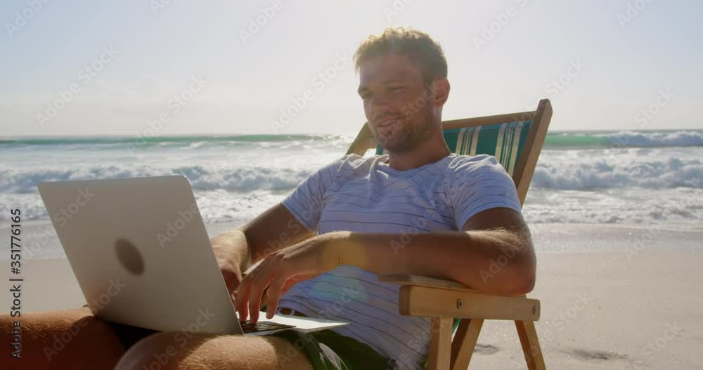 Man using laptop at beach in the sunshine