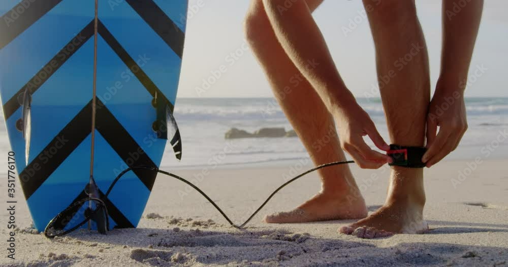 Man tying surfboard leash at beach in the sunshine Stock Video Adobe