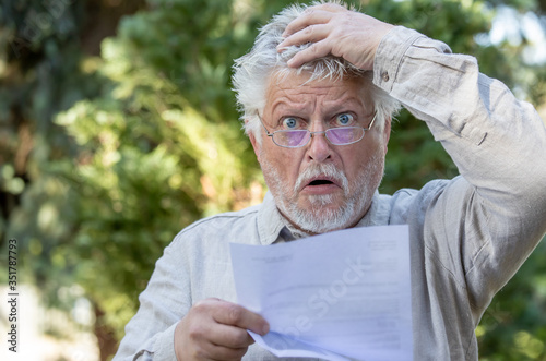 An older man reads a letter and is horrified. He wears glasses.