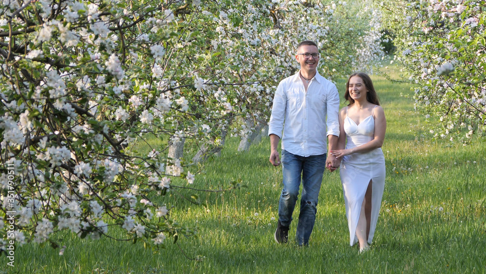 Fototapeta premium young guy and girl in blooming apple trees in the garden