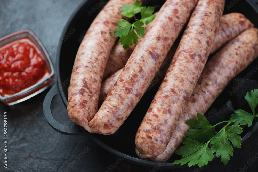Raw sausages made of pork and poultry in a cast-iron pan, selective focus, studio shot, close-up Raw sausages made of pork and poultry in a cast-iron pan, selective focus, studio shot, close-up
