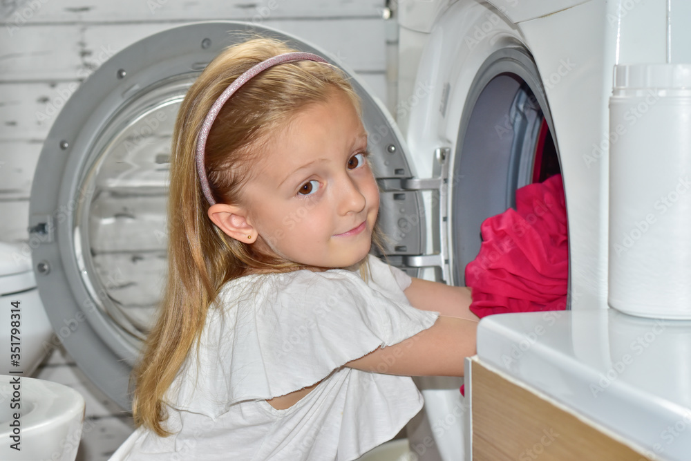 happy girl takes out colored things from a washing machine in the bathroom happy girl takes out colored things from a washing machine in the bathroom