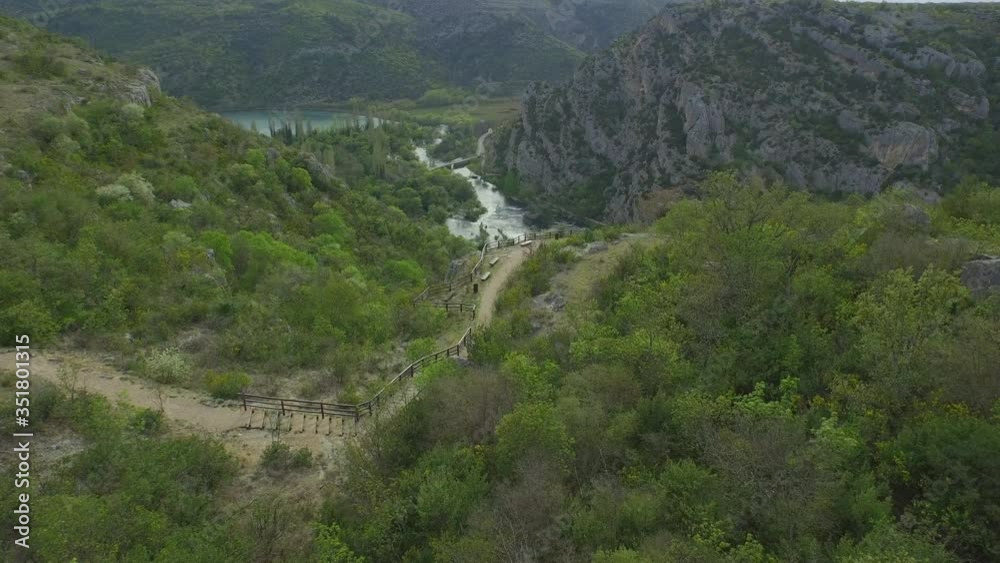 Aerial shot of trail amidst plants on mountain near river, drone flying forward over forest - Krka, Croatia Aerial shot of trail amidst plants on mountain near river, drone flying forward over forest - Krka, Croatia