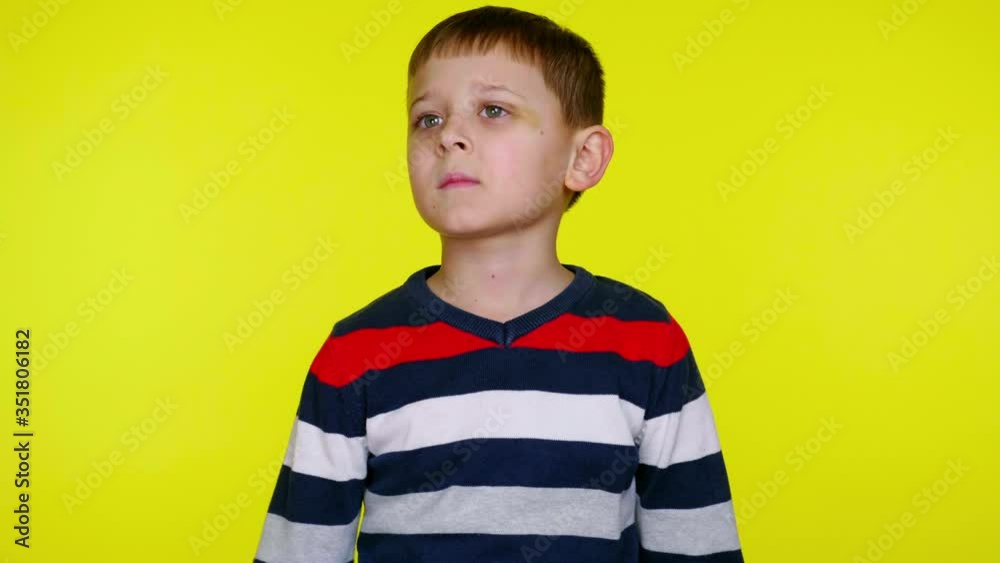 Confused child boy in a multi-colored sweater looks around and thinks what to choose by raising his hands up on a yellow background with copy space. Place for text or product. 4K slowmotion footage Confused child boy in a multi-colored sweater looks around and thinks what to choose by raising his hands up on a yellow background with copy space. Place for text or product. 4K slowmotion footage