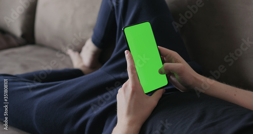 Closeup young man lying on a couch and using smartphone with green screen