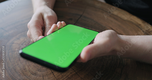 Closeup young man use smartphone with green screen while sitting at the table