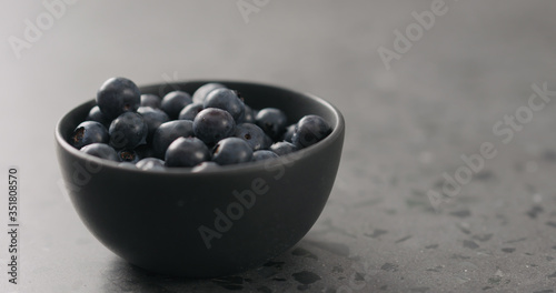 ripe blueberries in black bowl on concrete background with copy space