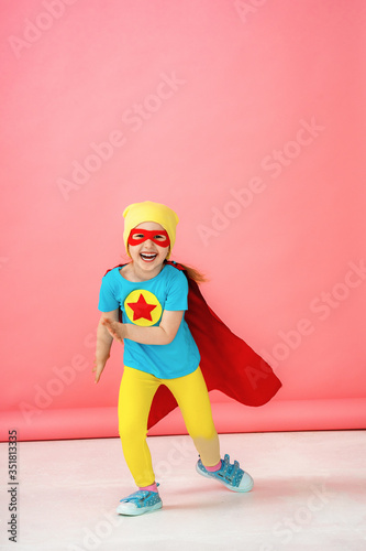 a little girl in a superhero costume, running forward on a pink background