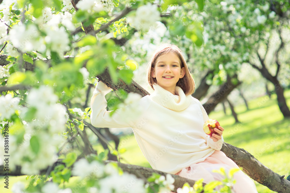 Happy beautiful teenage girl enjoying spring sunny day sitting on blossom tree ready to eat red delicious apple Happy beautiful teenage girl enjoying spring sunny day sitting on blossom tree ready to eat red delicious apple
