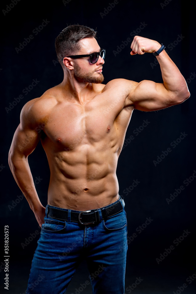 Brutal strong athletic men pumping up muscles. Workout and bodybuilding concept. Handsome man with naked torso. Fitness model is posing. Wearing sunglasses.