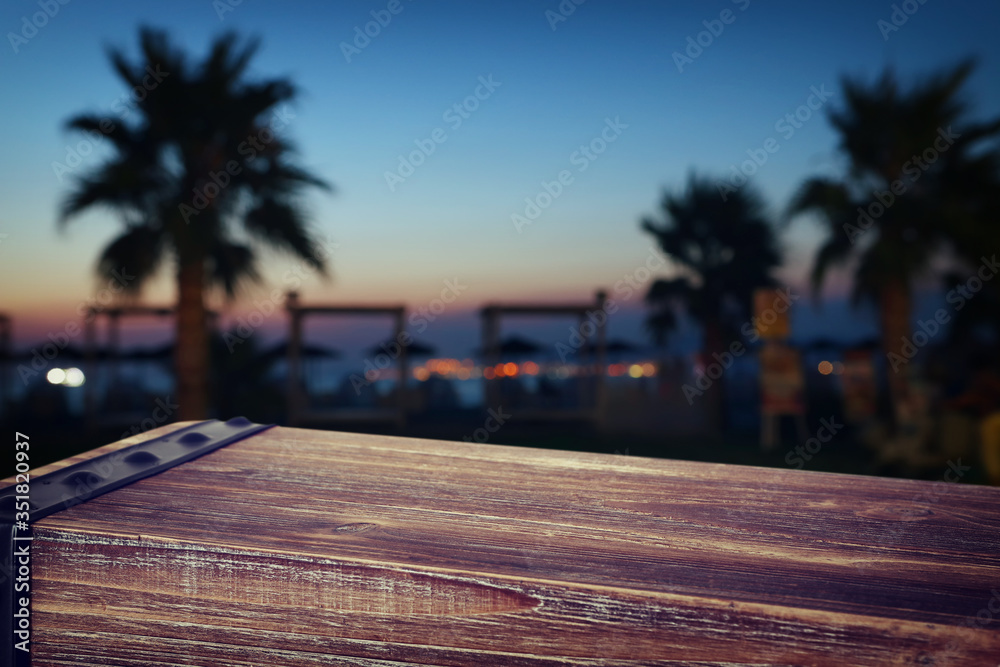 background Image of wooden table in front of abstract blurred tropical palms at sunset lights