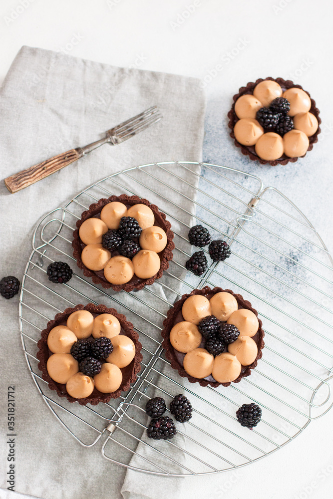 Blackberry tarts with whipped cream and chocolate filling on metal cooling rack. Grey background.