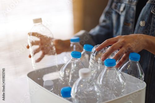 A woman collecting and separating recyclable garbage plastic bottles into a trash bin at home