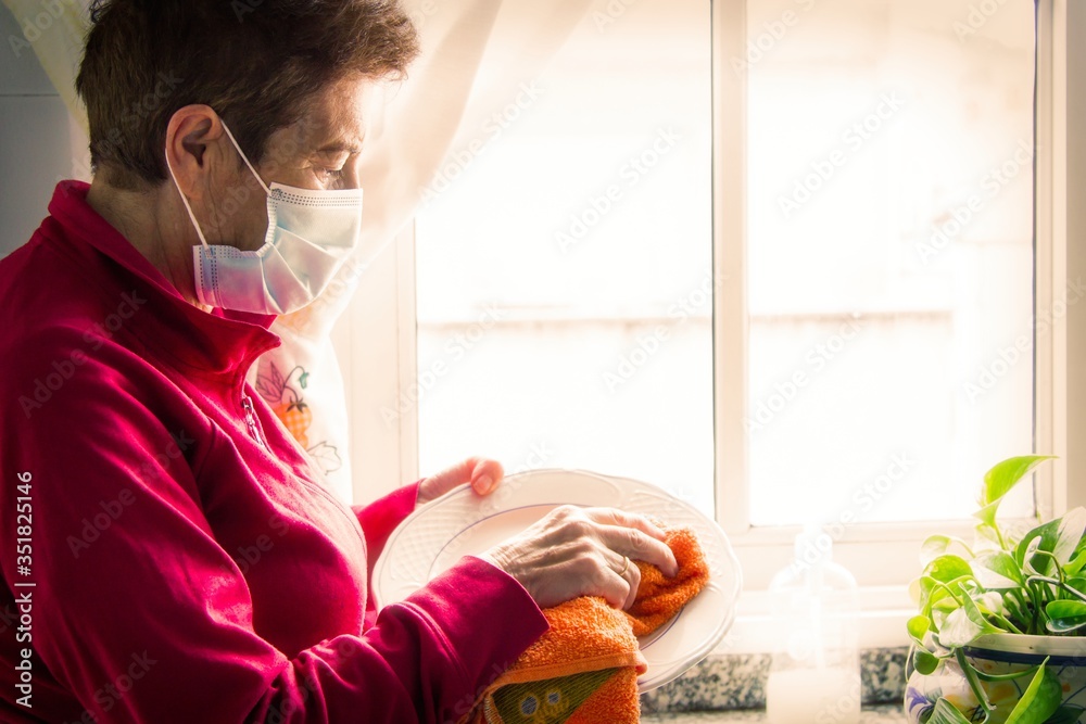 senior woman with medical mask cleaning dishes, preventive against viruses and infections senior woman with medical mask cleaning dishes, preventive against viruses and infections