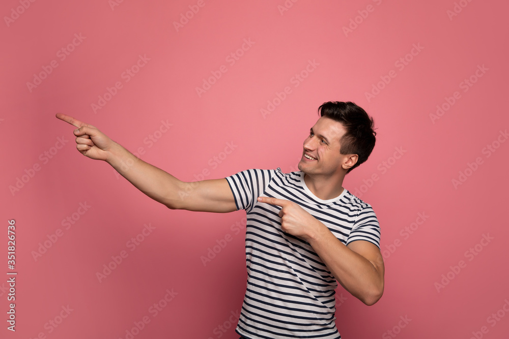 Looking to the left. Close-up photo of a strong man in a striped t-shirt, who is looking and pointing to the left with his both hands.