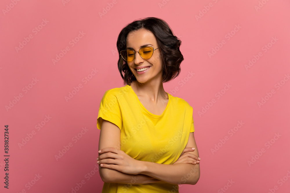 Lovely day. Close-up photo of content young woman in a yellow t-shirt and yellow sunglasses, who is standing with folded arms and smiling with her eyes closed. Lovely day. Close-up photo of content young woman in a yellow t-shirt and yellow sunglasses, who is standing with folded arms and smiling with her eyes closed.