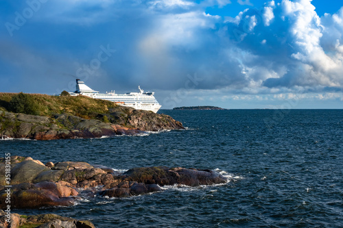 Cruise ship leaves the Harbor. A huge white ship against the rocky shore, water and sky. Sea travel by ship. Voyage. Travel by sea. The lainer is floating on gray water. Finland Helsinki. photo