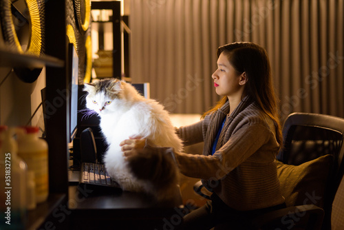 Young Asian woman holding pet cat while working from home