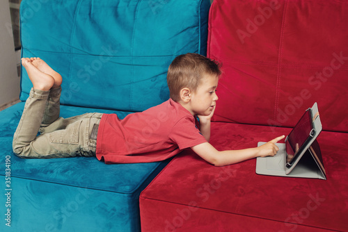 Photography Small boy is lying on the sofa and surfing on tablet