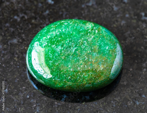 closeup of sample of natural mineral from geological collection - tumbled green Aventurine gem stone on black granite background from India photo