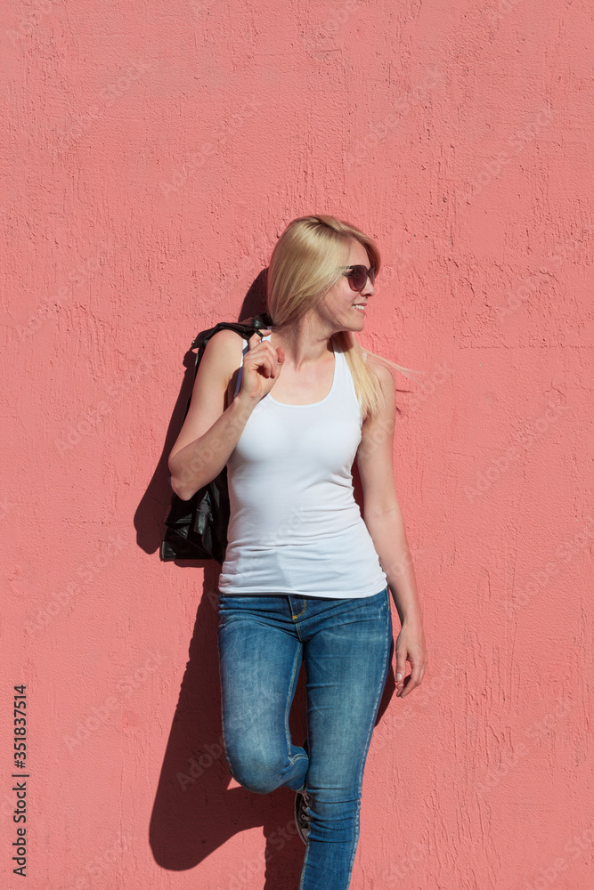 outdoor summer portrait of young blonde cheerful woman with sunglasses and white tank top against pink wall mock up tank top