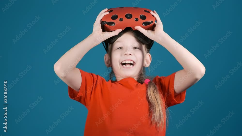 happy little girl takes off virtual reality goggles surprised by screen scene on blue background slow motion happy little girl takes off virtual reality goggles surprised by screen scene on blue background slow motion