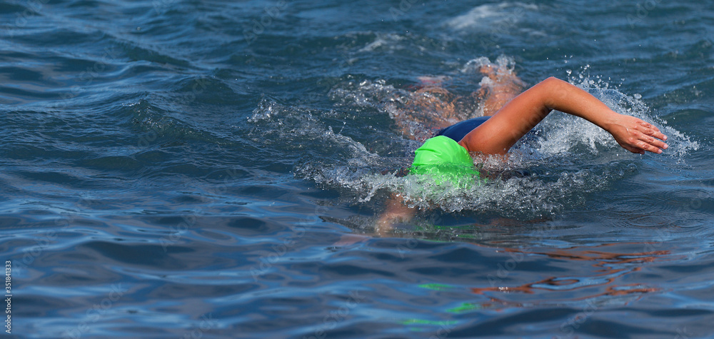 Triathlete woman swimming freestyle crawl in ocean, female triathlon swimmer swimming in professional triathlon