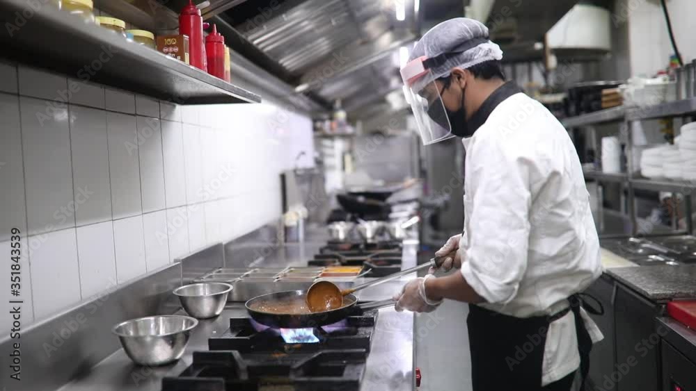 Chef cooking food in kitchen during quarantine lockdown with mask, gloves, shield and other safety protective gear. Chef cooking food in kitchen during quarantine lockdown with mask, gloves, shield and other safety protective gear.