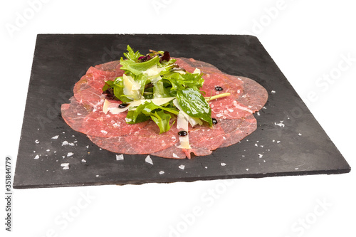 Gourmet Carpaccio with arugula, on a black stone plate, isolated on white background