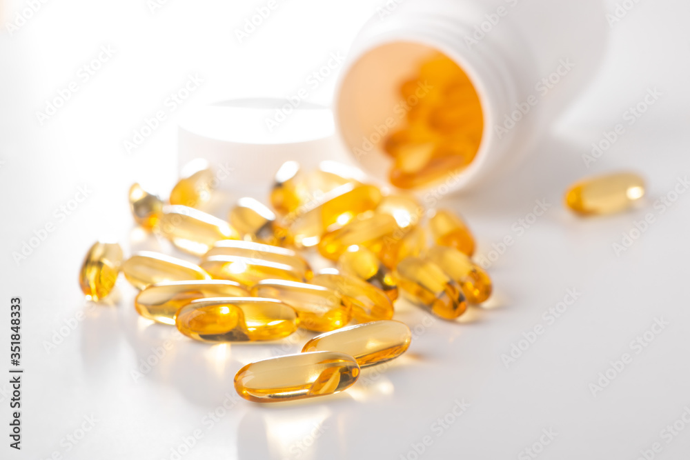 Yellow capsules scattered from a bottle on white background