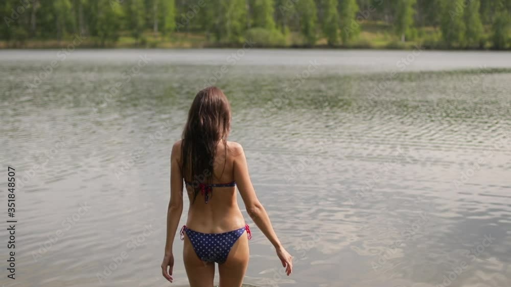 Beautiful woman comes into the water and swim, back view Beautiful woman comes into the water and swim, back view