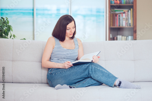 A casually dressed young woman reading on the couch in the living room.