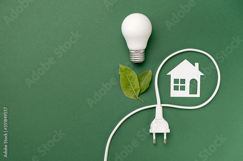 Concept for saving energy, eco-friendly, global warming. Creative top view flat lay of LED light bulb, electrical plug, leaves, paper house composition with copy space on green background photo