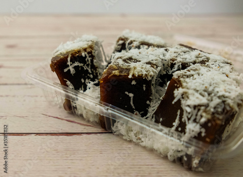 Close-up kaswi cake topped with grated coconut plate (brown steamed Malaysian dessert, combination of rice and tapioca flour, white sugar, alkaline water and dark palm sugar.) Wooden table. photo