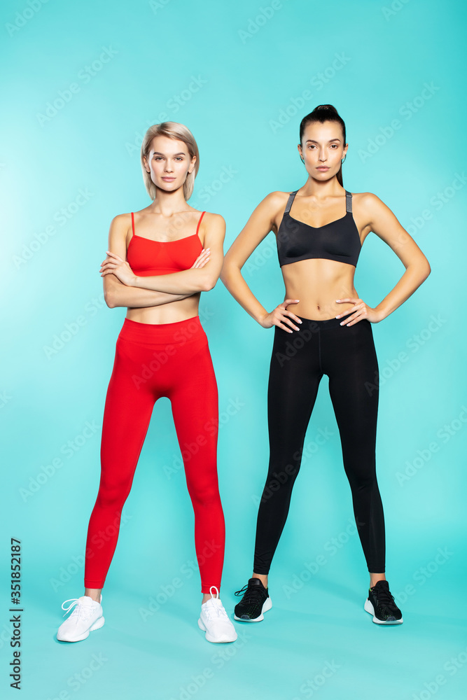 Fitness girls. Full length of two young and confident sporty girls in sportswear looking at camera while standing against blue background