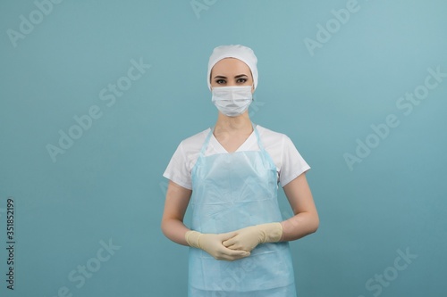 masked doctor in apron and gloves preparing for surgery on blue background