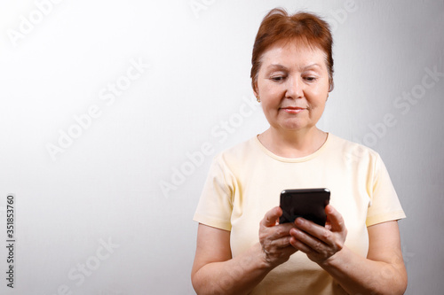 senior woman looks at the phone on a white background in a light T-shirt. place for text, isolated